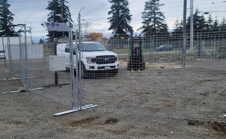 White truck and a small forklift vehicle enclosed in a lot protected by a portable wire fence 