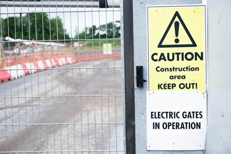 close up picture of a caution sign on the outside of a construction site fence 
